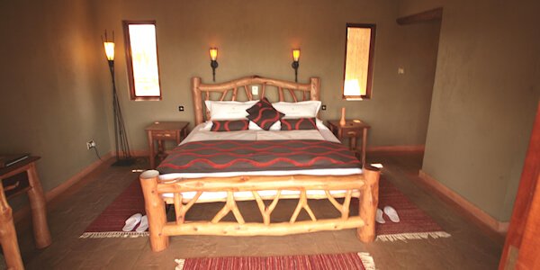 Junior Suites slaapkamer met openslaande deuren naar het terras en uitzicht op de drinkwaterplaats. Junior Suites slaapkamer met openslaande deuren naar het terras en uitzicht op de drinkwaterplaats, accommodatie Tsavo West Nationaal Park in Kenia